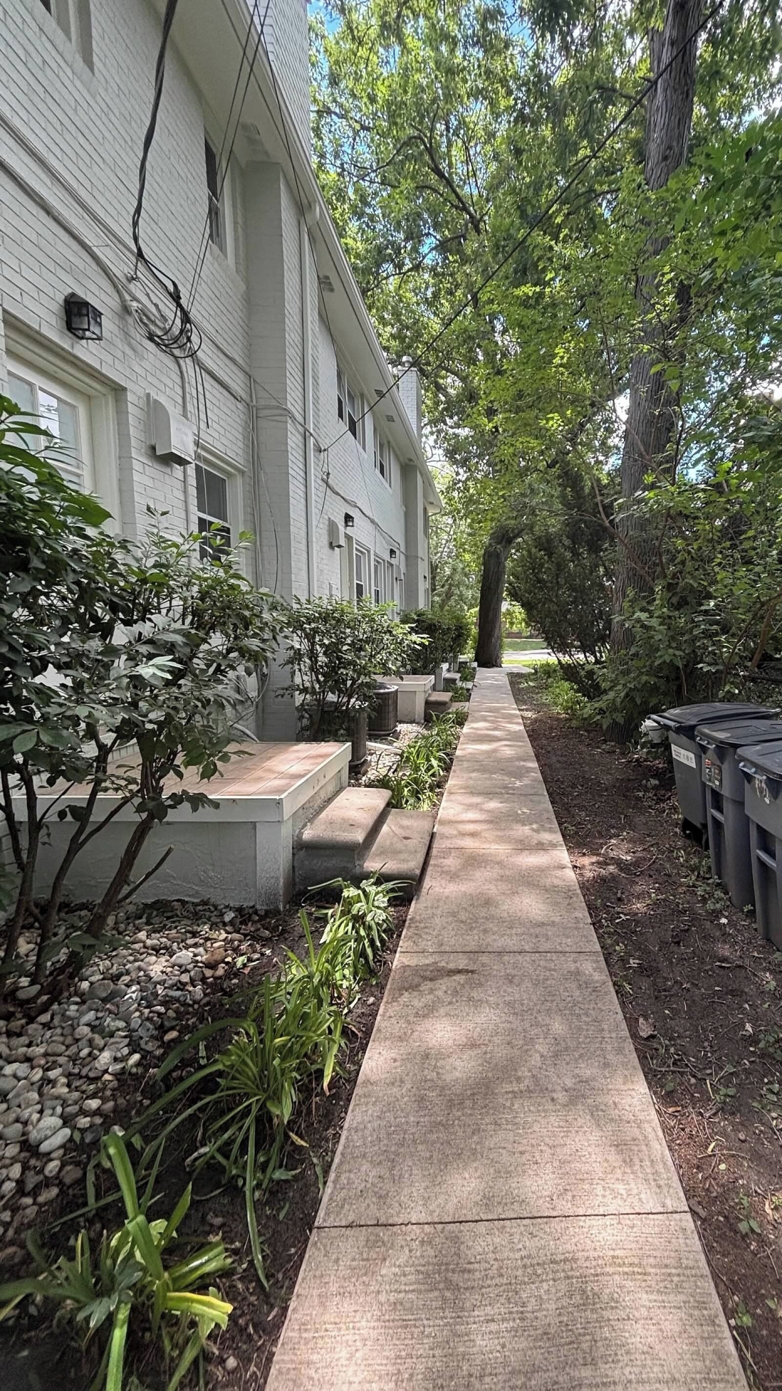 Un sendero conduce a un edificio de fachada de ladrillo, rodeado de follaje y árboles.