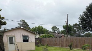 Ein Garten mit einer Holzterrasse, die zu einem Haus führt, einem Holzzaun und einer Rasenfläche.