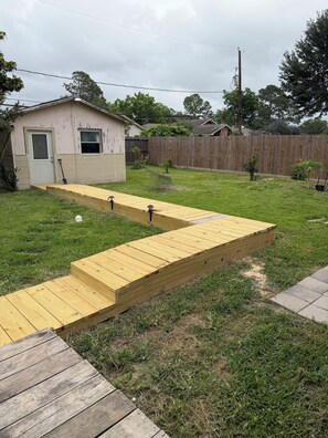 Ein Garten mit einer Holzterrasse, die zu einem Haus führt, einem Holzzaun und einer Rasenfläche.