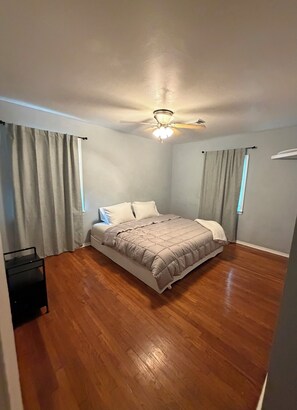 Ein Schlafzimmer mit einem Bett, einem Deckenventilator und einem Fenster mit Vorhängen.