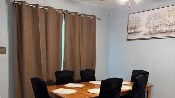 Ein Essbereich mit einem Holztisch, schwarzen Stühlen, einem Deckenventilator und einem Bild an der Wand.