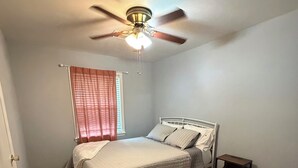 Ein Schlafzimmer mit einem Bett, Deckenventilator, einem Fenster mit Vorhängen und Holzboden.