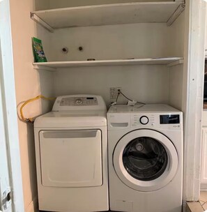 Ein Waschbereich mit einer Frontlader-Waschmaschine und einem Trockner, einem darüberliegenden Regal und einer Steckdose.