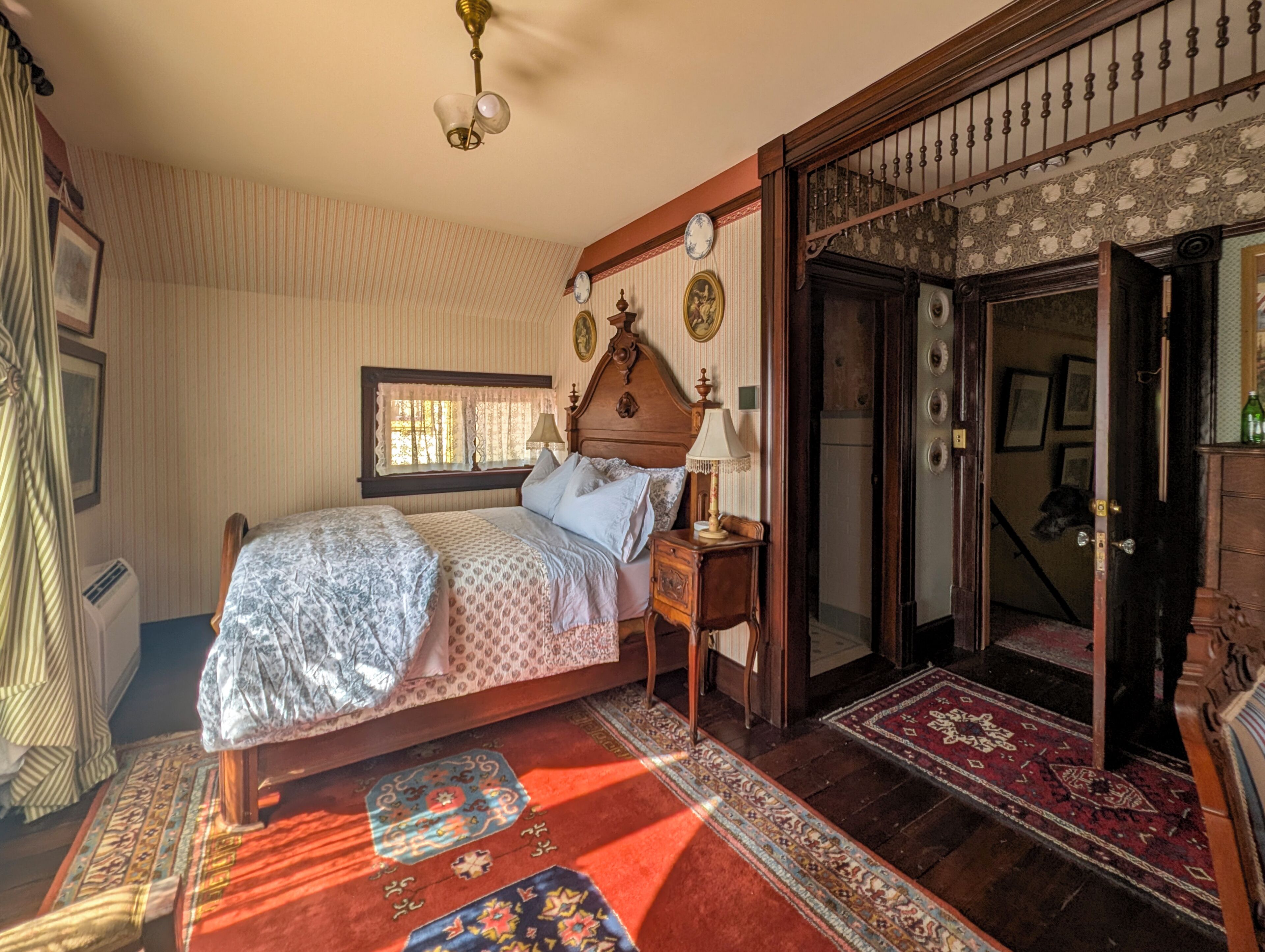 A traditional bedroom with a bed, bedside tables, a window, and a door leading to another room.