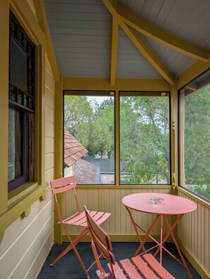 Una habitación con paredes amarillas, una ventana con vista a árboles y una mesa rosa con un vaso.