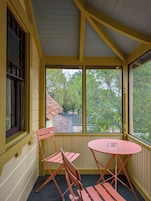 Una habitación con paredes amarillas, una ventana con vista a árboles y una mesa rosa con un vaso.