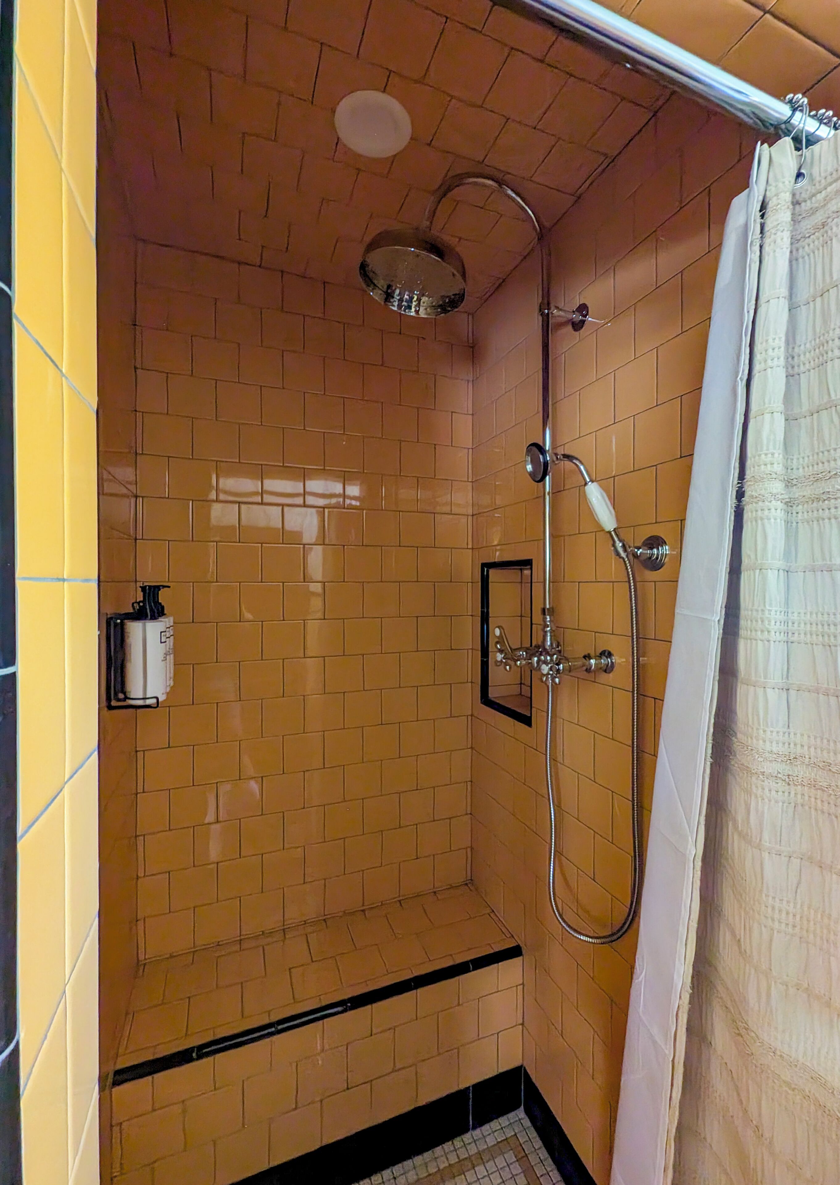 Un área de ducha con paredes de azulejos, un cabezal de ducha, un rociador manual y un perchero para toallas.