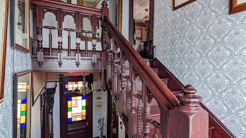 Una imponente escalera con ornamentada carpintería, que conduce a un espacio con un vitral y obras de arte enmarcadas en las paredes.