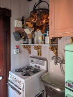 Cocina antigua con estufa, pileta y ollas colgando.