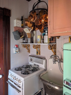 Cocina antigua con estufa, pileta y ollas colgando.