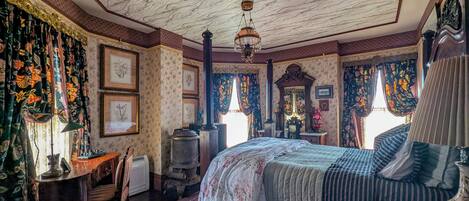 A room with a large bed, a wooden chair, a desk, and a patterned carpet.