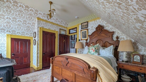 A bedroom with a wooden bed, a nightstand with a lamp, a dresser, and a door with a decorative handle.