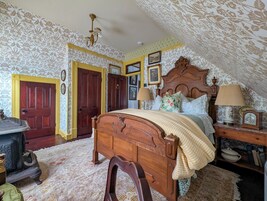 Un dormitorio con una cama de madera, una mesita de noche con lámpara, un aparador y una puerta con picaporte decorativo.