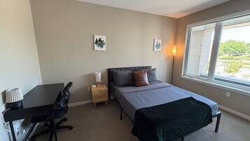 Un dormitorio con cama, mesita de noche, lámpara, silla y ventana con vistas.