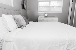 A bedroom with a bed, pillows, a bedside table with a mirror, and a dresser.