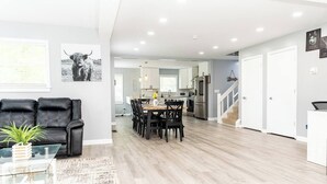 Ein modernes Wohnzimmer mit einer schwarzen Ledersofa, einem Glastisch und einem Essbereich mit Holztisch und Stühlen.