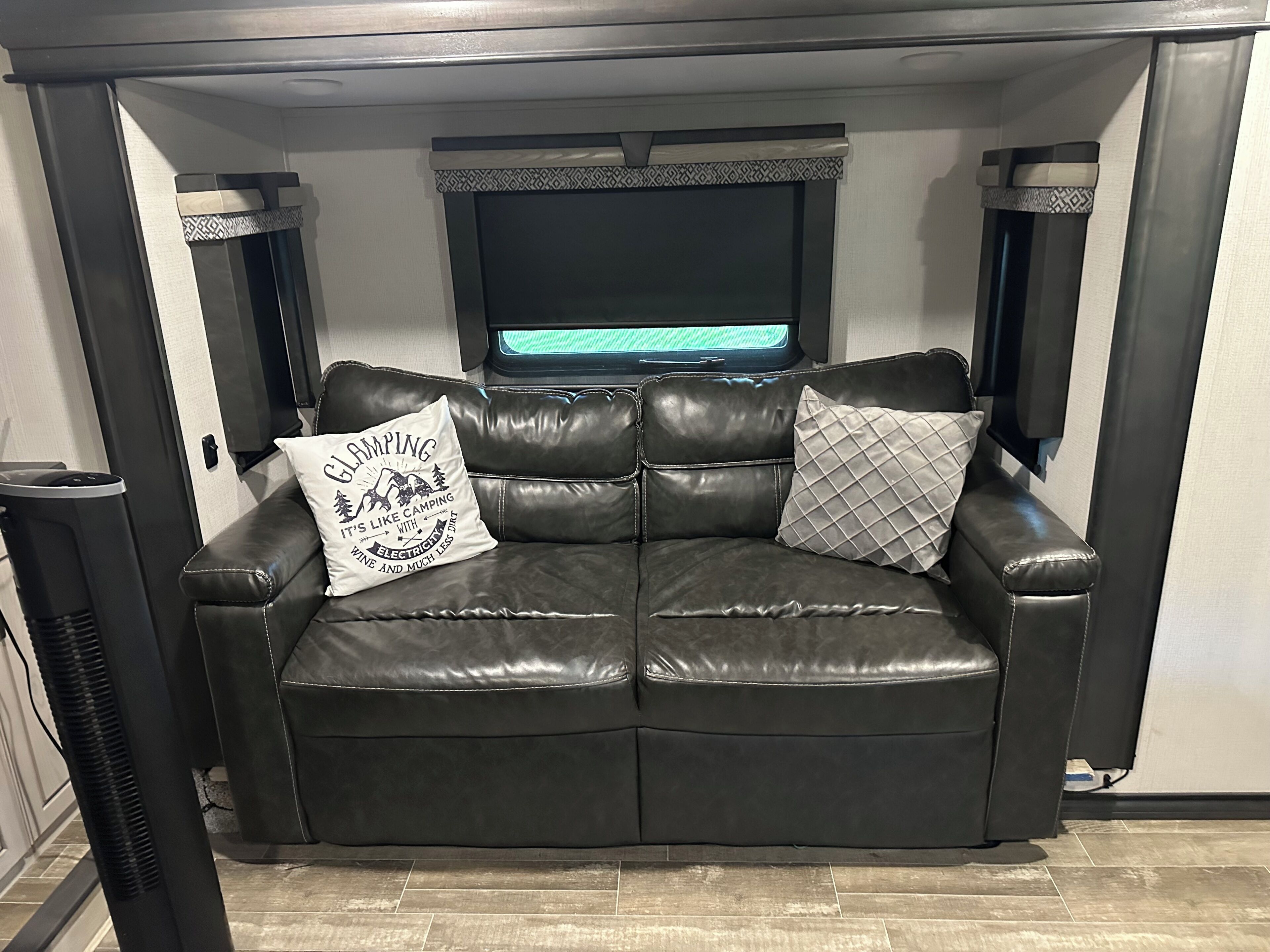 A black leather sofa with two decorative pillows and a flat-screen TV mounted above it.