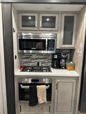 A compact kitchen with a stainless steel microwave, gas stove, and oven.