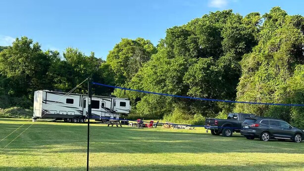 A grassy field with a white RV and a black SUV parked, surrounded by trees. - Glamping in Rock Island (Walling)