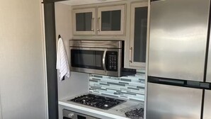 A compact kitchen with a stainless steel refrigerator, a microwave, an oven, and a sink. - Glamping in Rock Island (Walling)