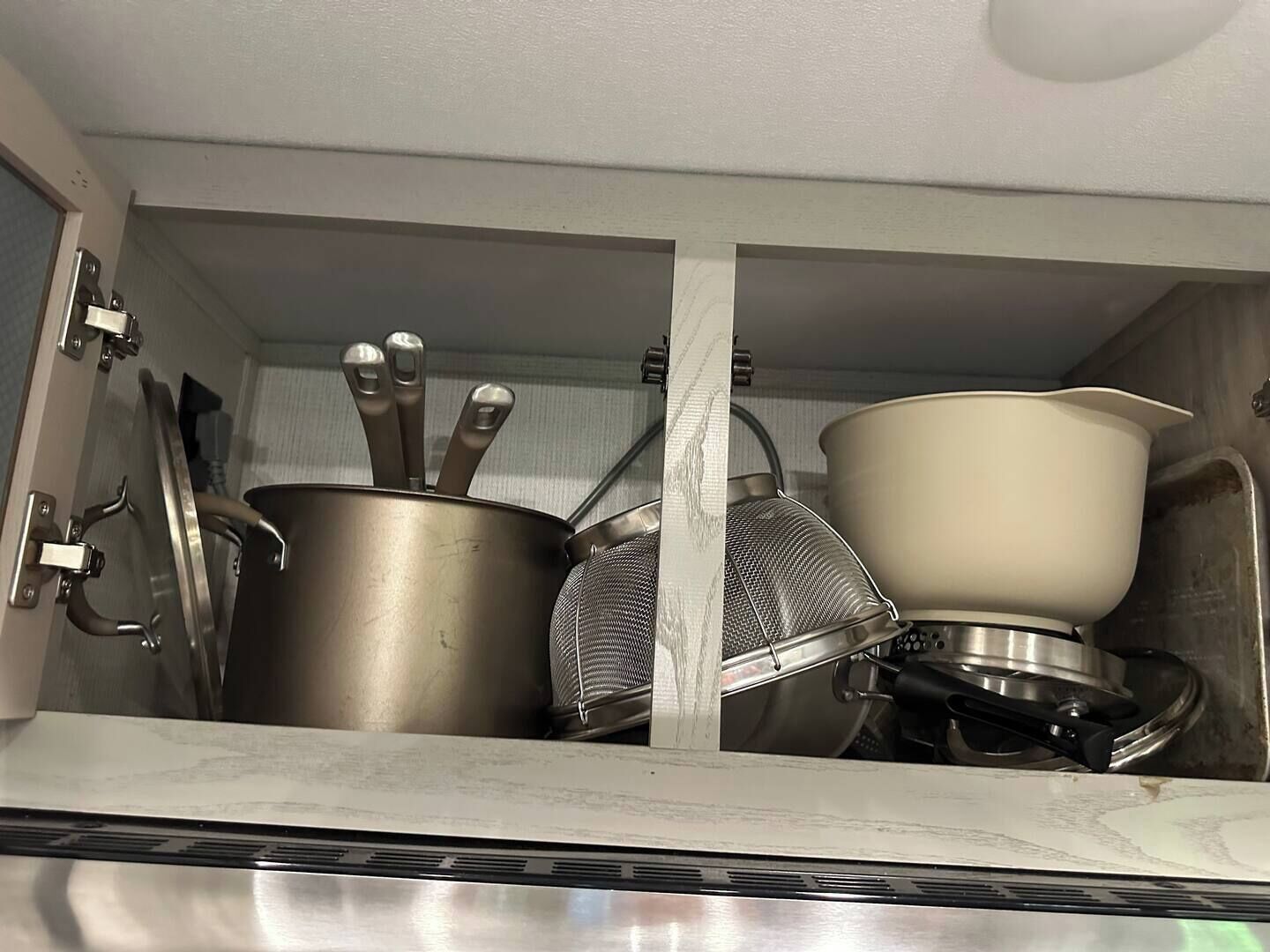 A kitchen with stainless steel cookware, including pots and a strainer, and a white pot on the counter.