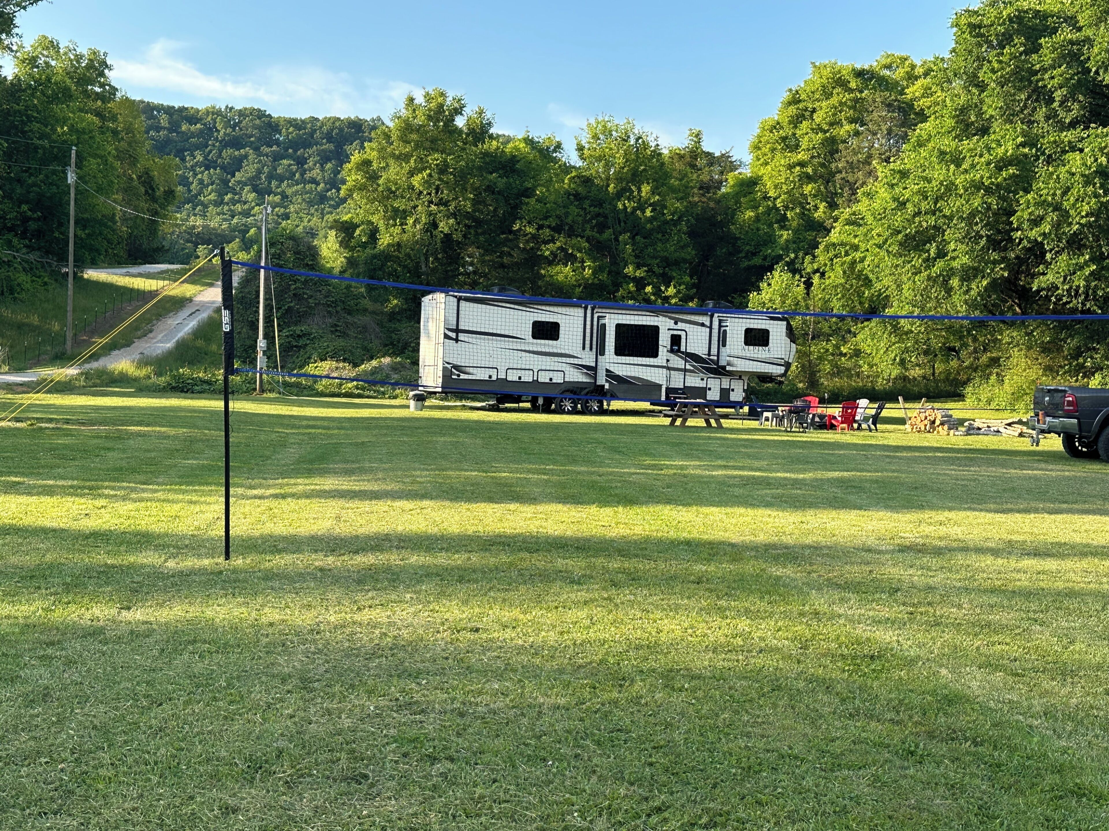 A large RV parked in a grassy field with a forested hill in the background.