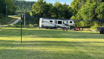 A large RV parked in a grassy field with a forested hill in the background.