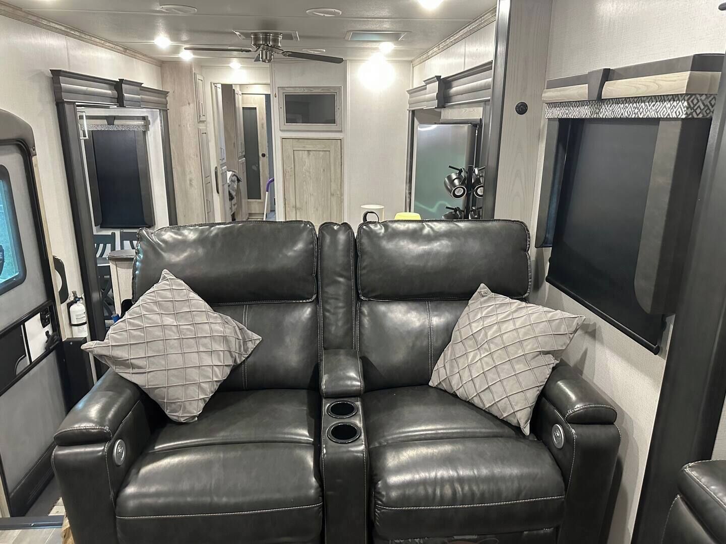 A black leather sofa with quilted pillows in a well-lit room with a ceiling fan, a large mirror, and a flat-screen TV.