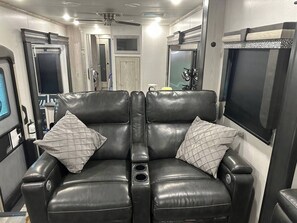 A black leather sofa with quilted pillows in a well-lit room with a ceiling fan, a large mirror, and a flat-screen TV.