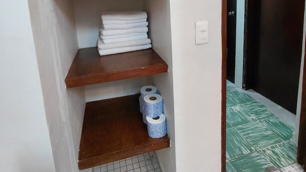 Et badeværelse med en træhylde med håndklæder og toiletpapir.