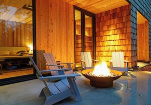 A modern wooden cabin with a fire pit, outdoor seating, and a visible bedroom.