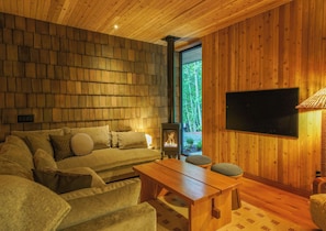 A cozy living room with a wooden ceiling, a flat-screen TV mounted on the wall, a sofa set, and a fireplace.
