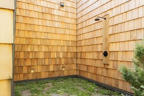 A corner of a building with wooden siding and a black metal structure, possibly a door or window frame. - New-Cedar House-Your Private Coastal Retreat! (Ucluelet)