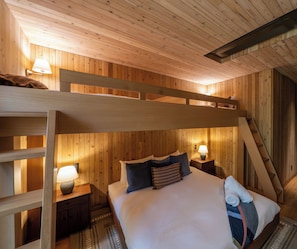 A bunk bed room with wooden walls, a nightstand with a lamp, and a bed with pillows.