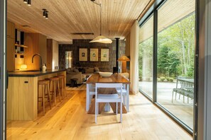 A modern kitchen with wooden flooring, a dining area with a table and chairs, and a large window offering a view of the outdoors.