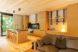 A modern kitchen with wooden cabinets, a central island, and bar stools. - New-Cedar House-Your Private Coastal Retreat! (Ucluelet)