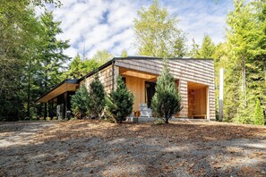 A modern wooden cabin with a covered porch, surrounded by trees and a gravel driveway. - New-Cedar House-Your Private Coastal Retreat! (Ucluelet)