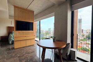 A modern living room with a large TV, a dining table, and a view of a cityscape through large windows. - Suite de lujo, Jacuzzi y Alberca | Punto São Paulo (Guadalajara)