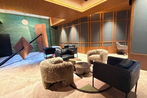 Un intérieur moderne avec un plafond en bois, un mur d’accent vert et un coin salon comprenant un canapé noir et des fauteuils moelleux.
