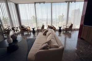 A modern living room with a sofa, chairs, a coffee table, and a view of a cityscape through large windows. - Suite de lujo, Jacuzzi y Alberca | Punto São Paulo (Guadalajara)