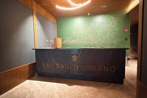 Eine Rezeption mit der Aufschrift 'SAO PAULO URBANO', eine Wand mit grünen Fliesen und einer Karte sowie eine Holzbodenleiste.