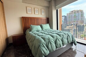A bedroom with a bed, a nightstand, a wooden headboard, and a city view through a large window. - Suite de lujo, Jacuzzi y Alberca | Punto São Paulo (Guadalajara)