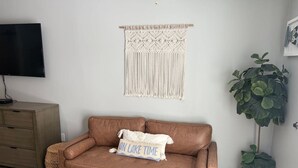 A living room with a brown leather sofa, a macrame wall hanging, a flat-screen TV, a wooden cabinet, and a potted plant. - Victorian Inn #226 | 2 Queen Beds (Elkhart Lake)