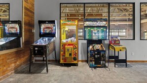 A row of arcade machines in a room with a wooden floor and a window with a view of the roof structure. - Victorian Inn #226 | 2 Queen Beds (Elkhart Lake)