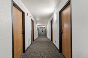 A hotel hallway with carpeted floors, wooden doors, and light fixtures.