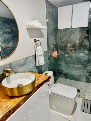 Ein Badezimmer mit Marmorwand, einem runden Waschbecken mit Holzauskładung, einer Toilette und einer Duschkabine aus Glas.