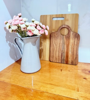 A white ceramic pitcher with pink and white flowers on a wooden surface next to a wooden cutting board. - Wood & White (Hialeah)