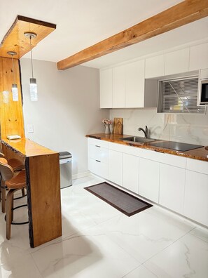 A modern kitchen with white cabinets, a wooden bar counter, and a built-in stove. - Wood & White (Hialeah)