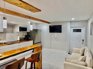 A modern kitchen with a wooden ceiling, white cabinets, a stainless steel refrigerator, a microwave, and a bar area with a wooden countertop and two wooden chairs. - Wood & White (Hialeah)