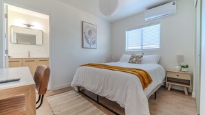 Una camera da letto moderna con un letto, un comodino, una lampada e una finestra con persiane.